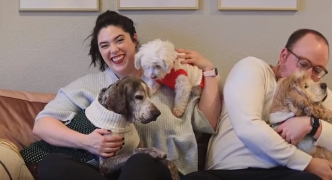 woman and man sitting with three dogs